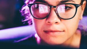 Close up of a woman wearing glasses with the word AI reflected on the glass.