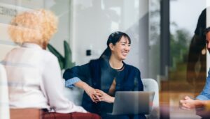 Woman sitting in a business meeting, listening to someone talking. She is smiling.