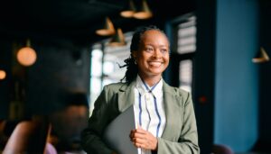 Woman smiling and holding a laptop under her arm