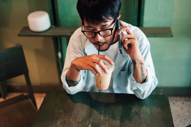 Young man drinking an iced coffee while on the phone