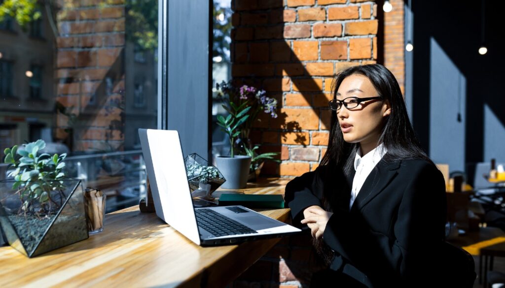 Young woman sitting in a casual, sunny workspace working on a laptop
