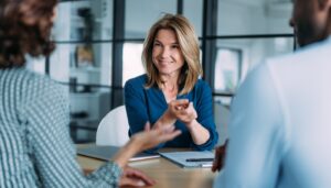 Woman sitting at a table in a meeting. She is smiling.